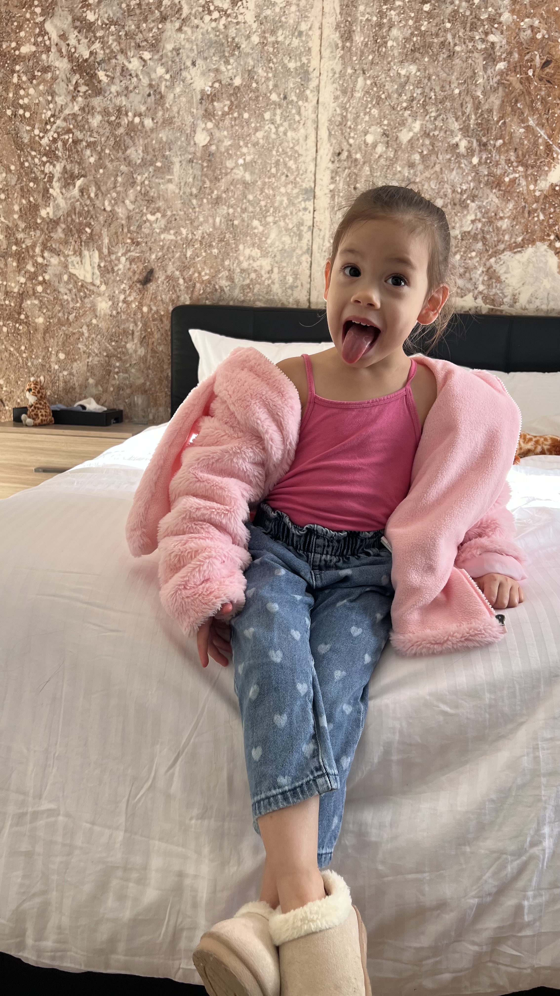 Kiara sitting on a bed, pulling a playful face with her tongue out.